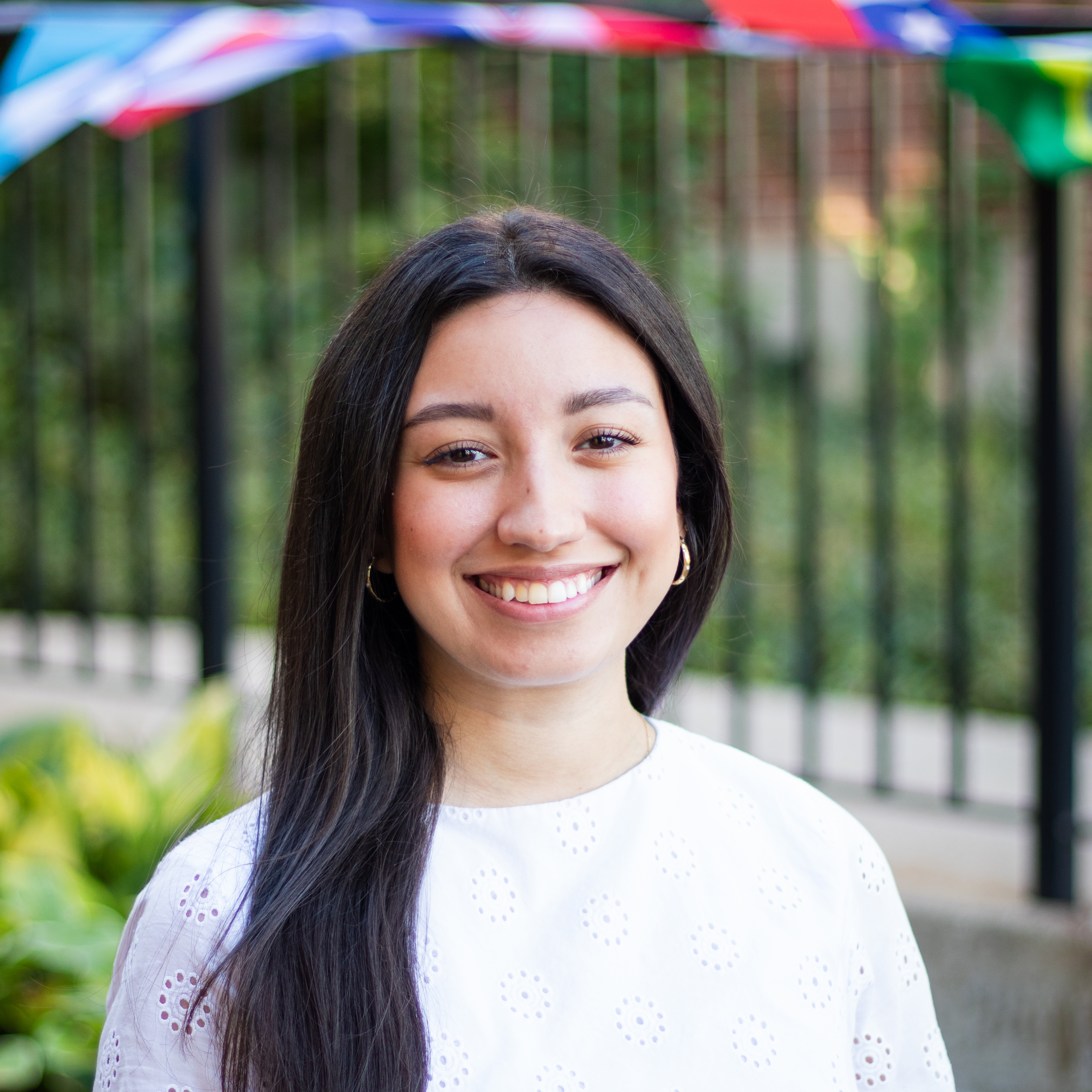 Headshot of Cynthia Diaz, a woman with long black hair and white blouse smiling against a landscape of campus
